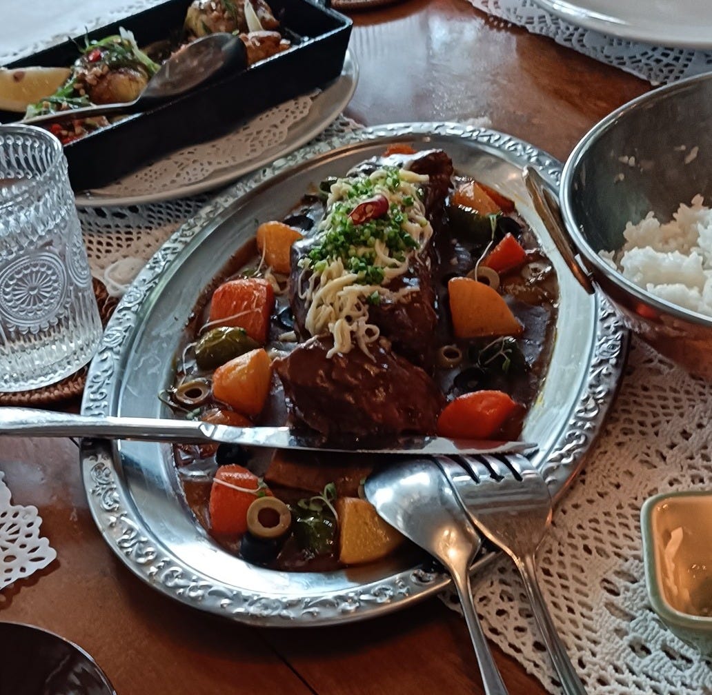 a platter of beef caldereta with potatoes, carrots, olives, and cheese topping