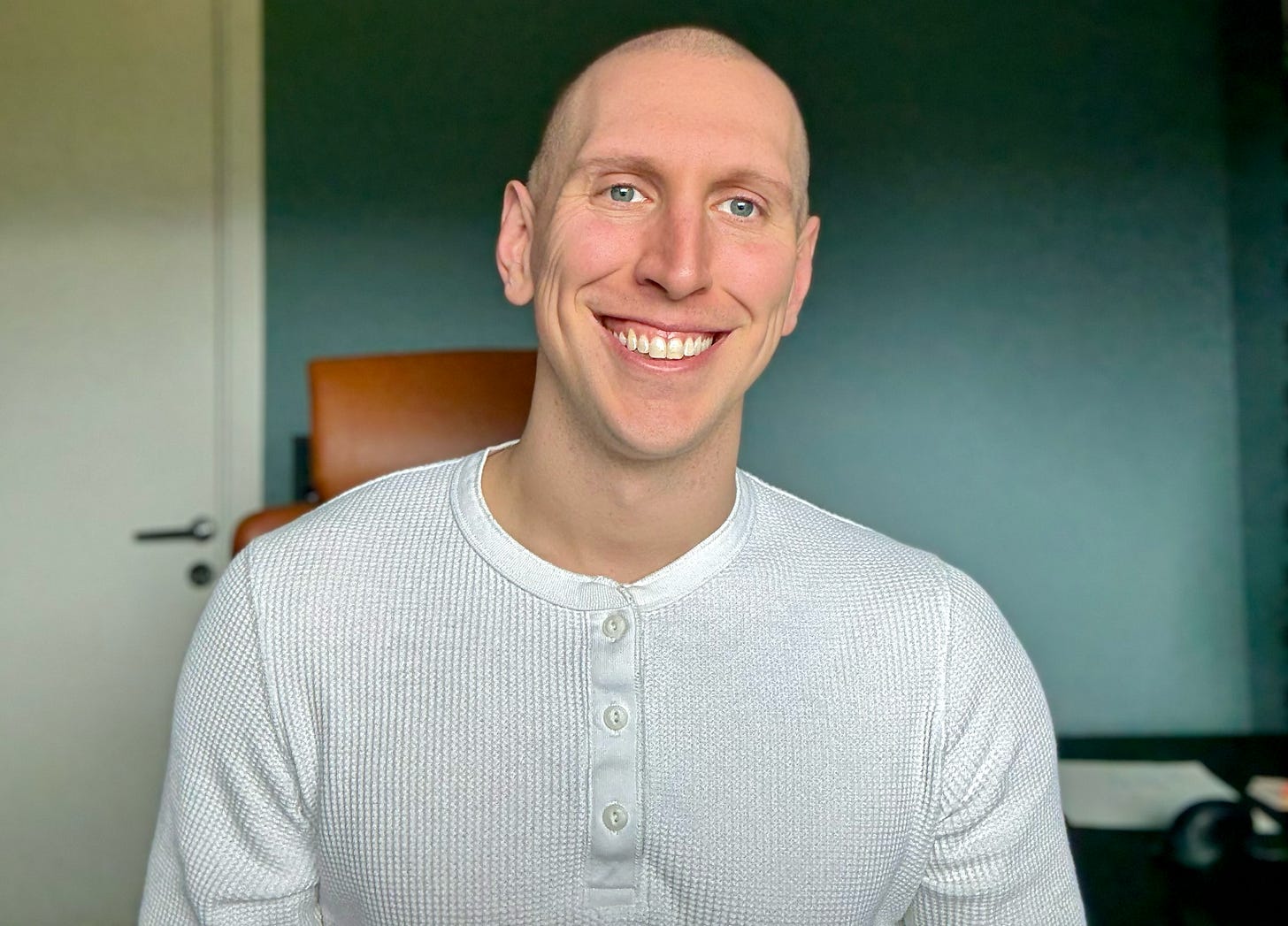 Dominik Gmeiner smiling with a shaved head sitting in his office.