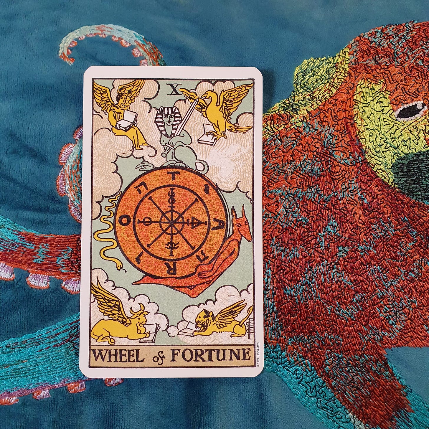 Wheel of Fortune tarot card from a Rider-Waite-Smith style deck on embroidered blue bird fabric for Tarot DMs.