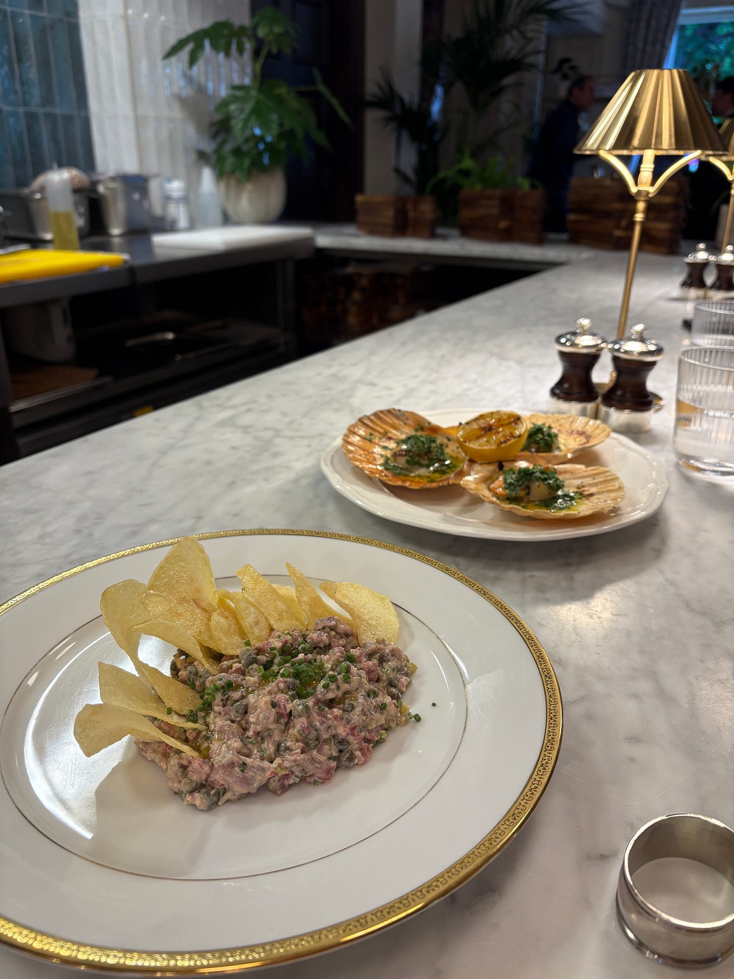 A mound of steak tartare with crisps in the foreground, three scallops in the background A mound of steak tartare with crisps in the foreground, three scallops in the background