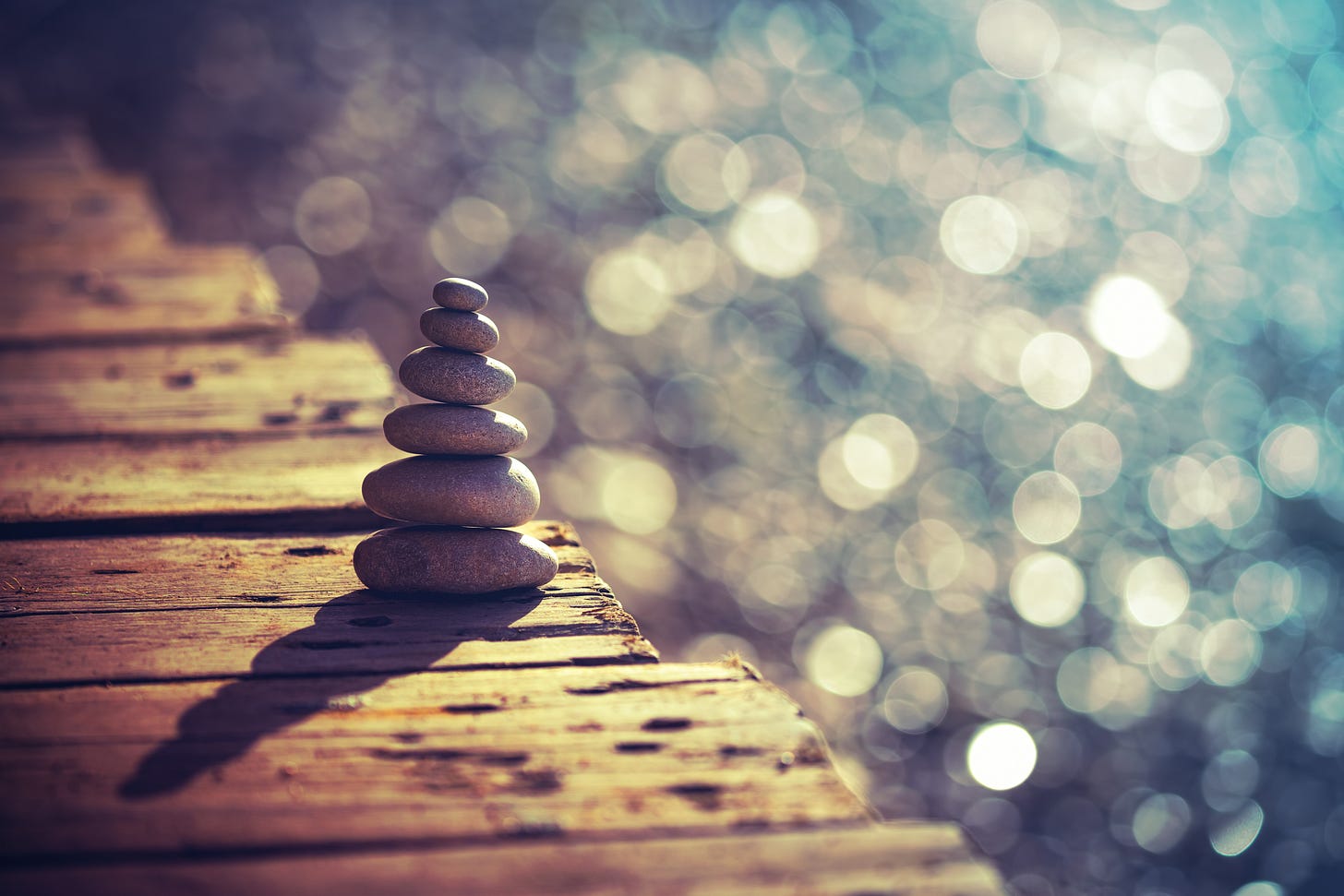 a stack of stones sitting on a wooden dock beside sparkling water, the stones are stacked in descending order of size