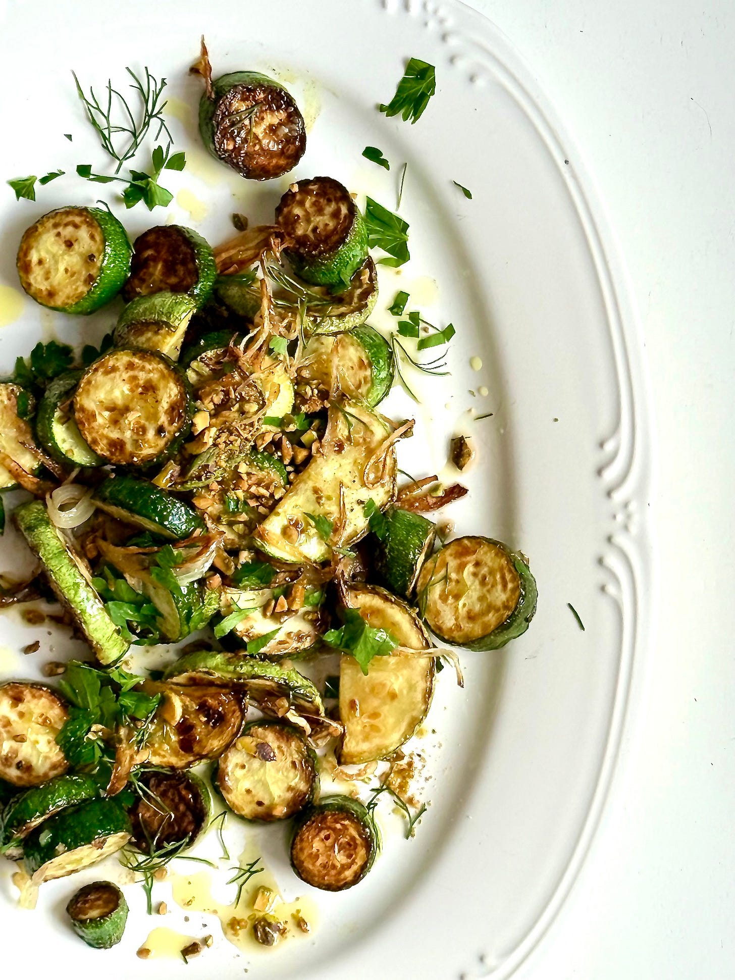 a white platter with sauteed zucchini and fresh herbs. 