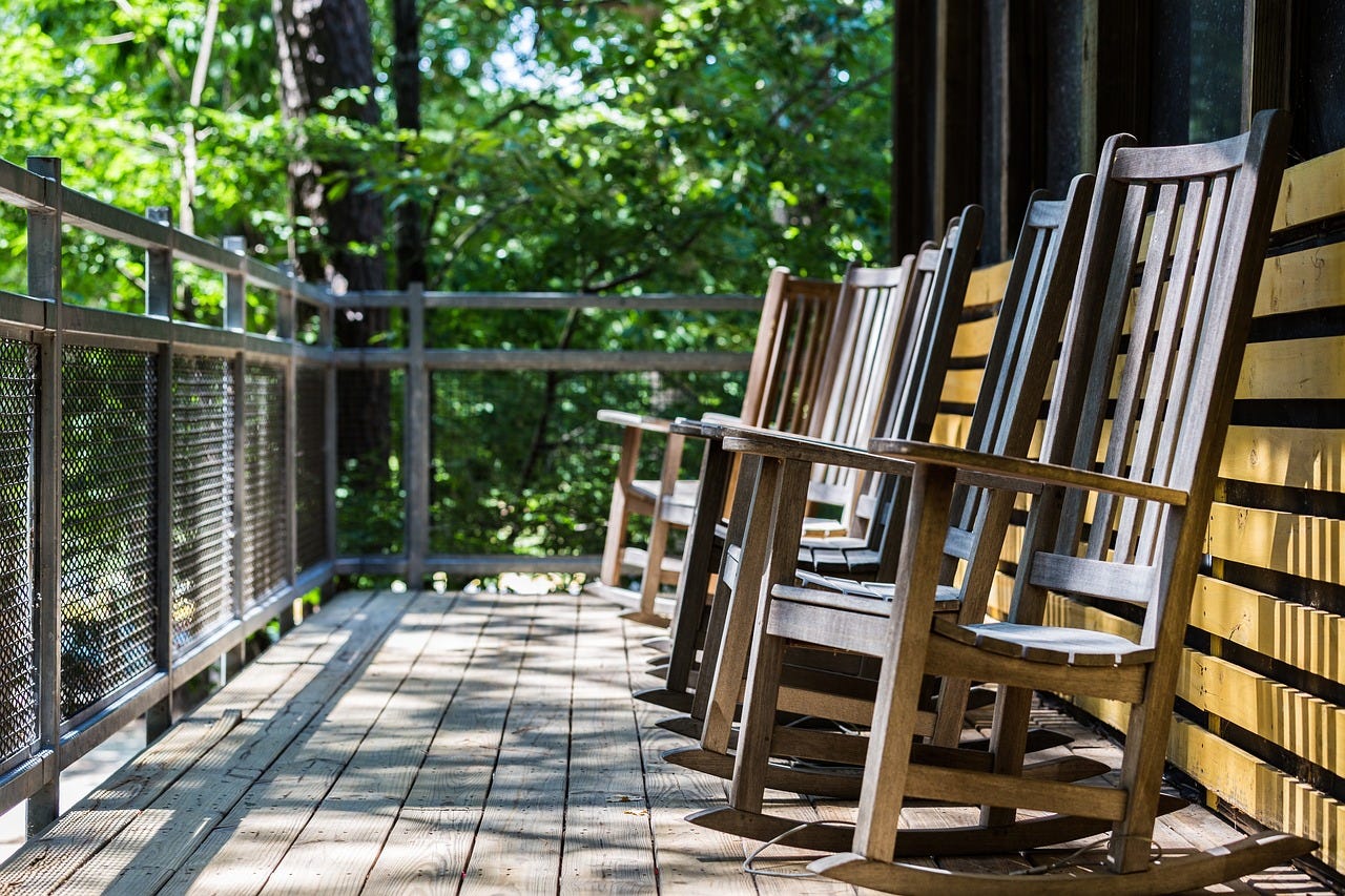 rocking chairs on a porch surrounded by green foliage