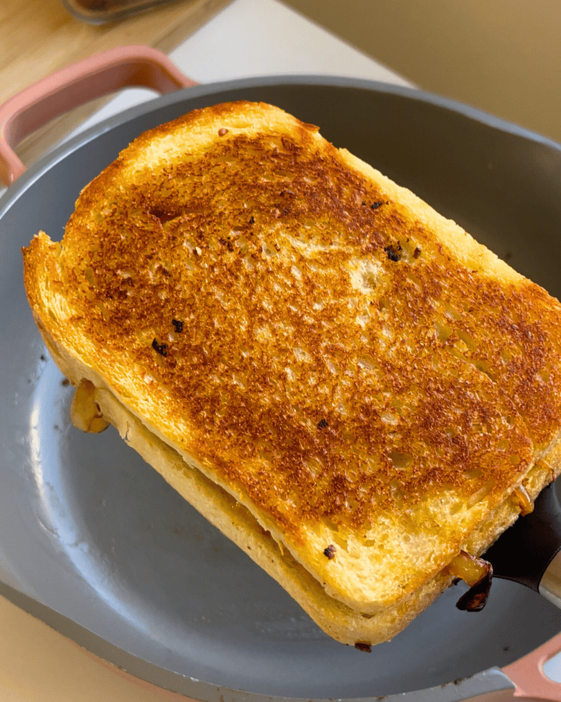 a grilled cheese sandwich on a spatula held above a grey frying pan