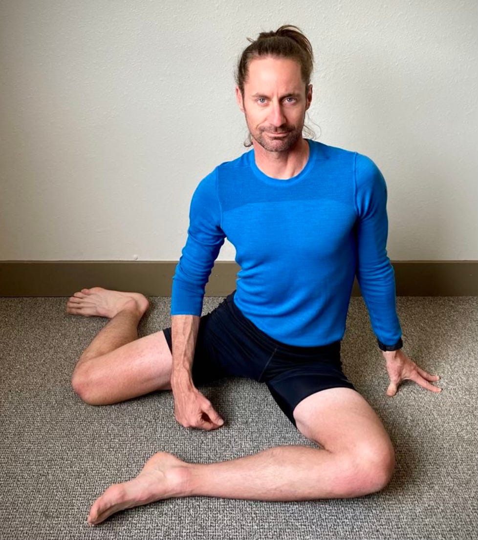 A man doing a hurdler hip stretch on the floor