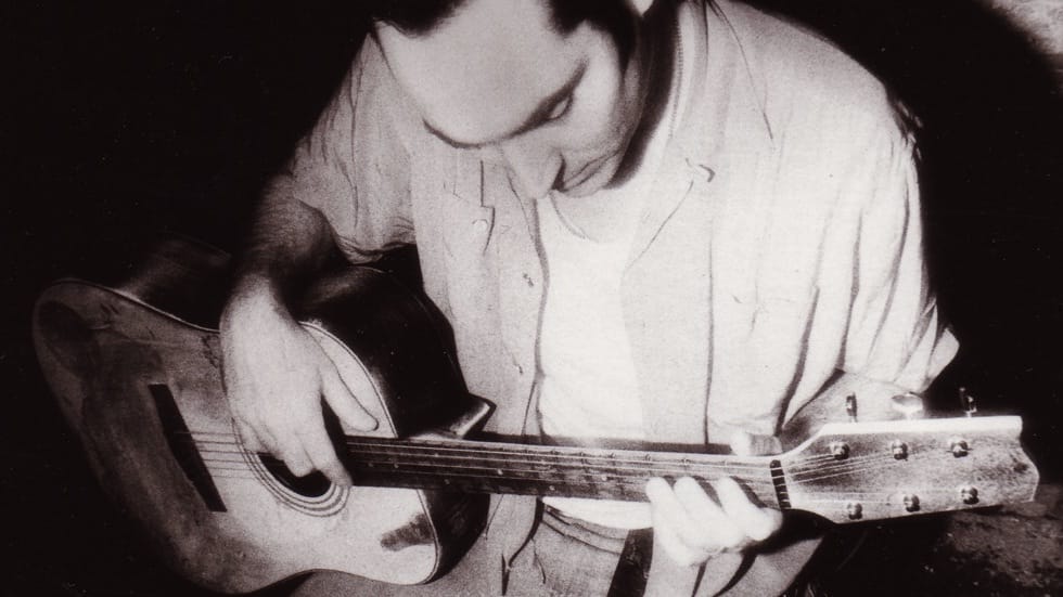 Black and white photo of Michael Knott looking down at an acoustic guitar Black and white photo of Michael Knott looking down at an acoustic guitar