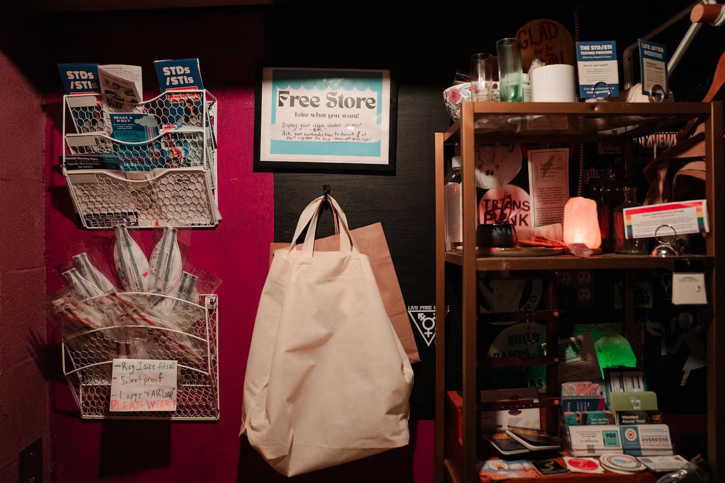 A little corner in the bar where there's a small shelf with some items on it and a couple of baskets hanging on the wall with pamphlets and other materials. A sign in the middle of the wall says "free store."