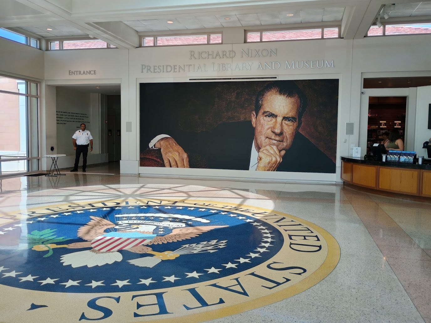    Huge portrait of Richard Nixon (head and shoulders) resting one hand under chin, one arm on furniture, under sign for Richard Nixon Presidential Library and Museum