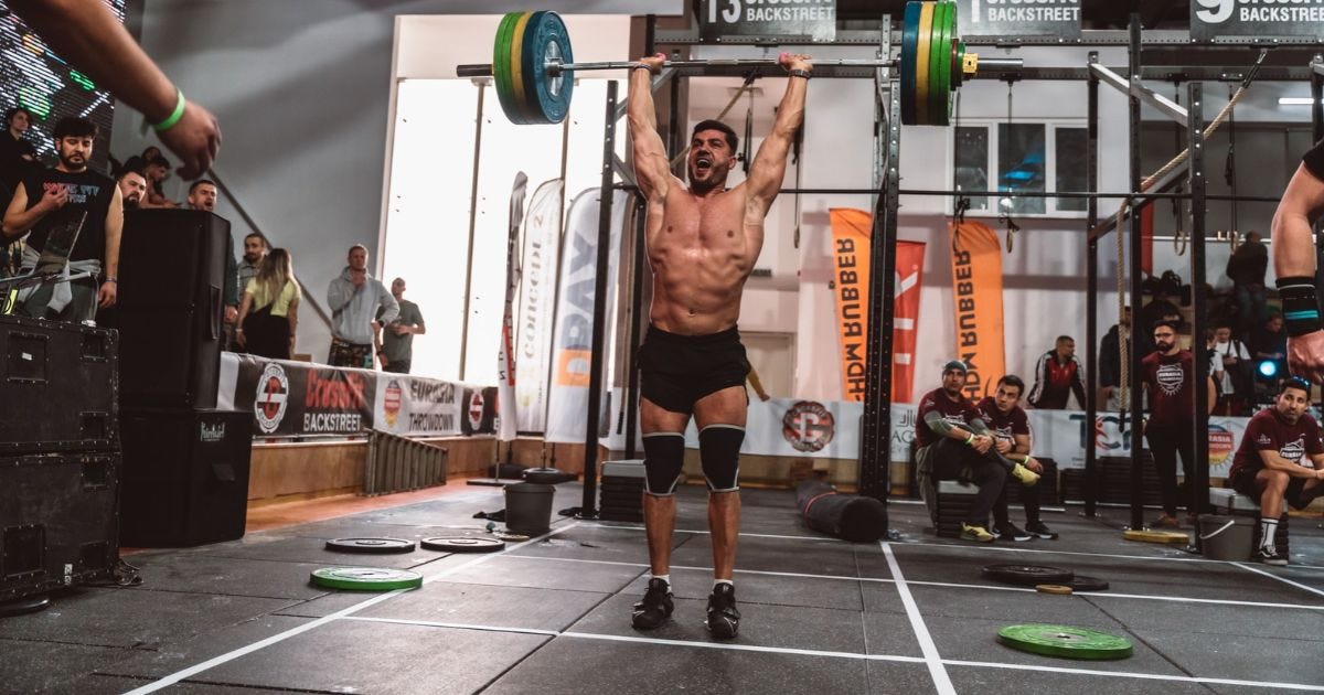 A muscular athlete performs a powerful overhead lift during a CrossFit competition indoors, showcasing strength and determination A muscular athlete performs a powerful overhead lift during a CrossFit competition indoors, showcasing strength and determination
