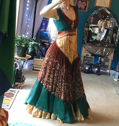 Gallery of sparkly costumes and costuming supplies, two wigs in golden brown on mannequin heads, and gold-leaf leather in a pile on the floor.