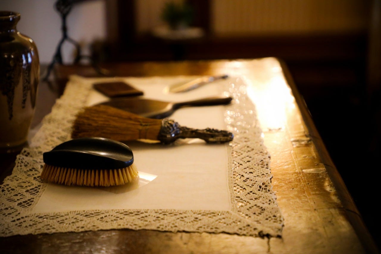 Brushes, mirrors and combs rest on a white laced doily, on a dark wooden table.