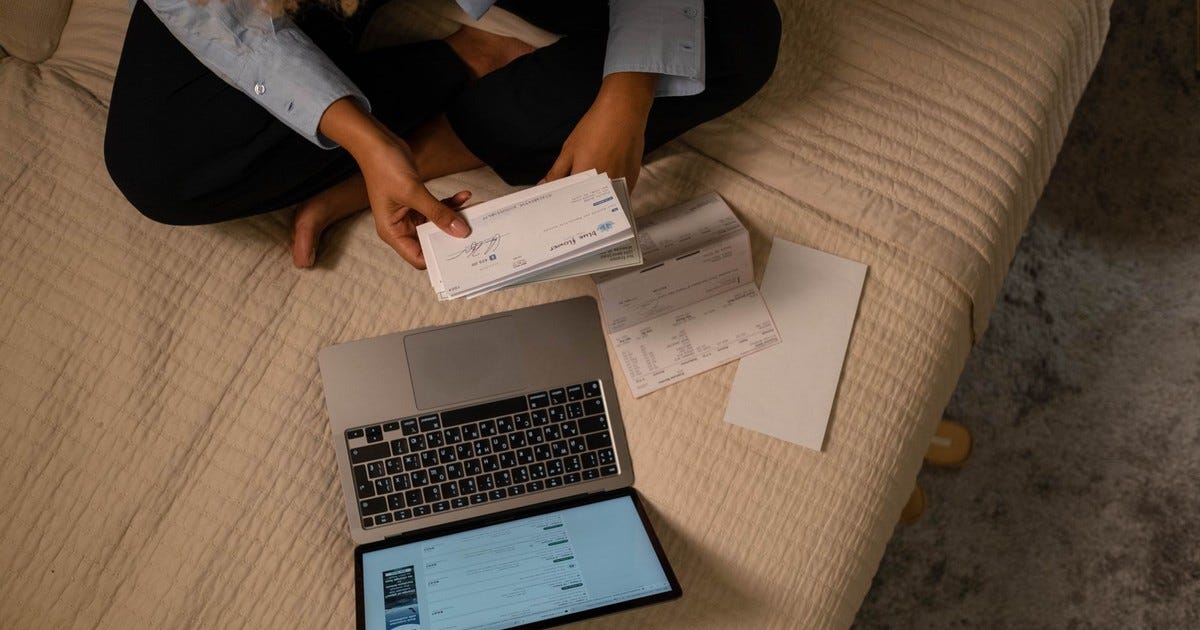 Overhead view of woman organizing finances on bed with laptop and checks.