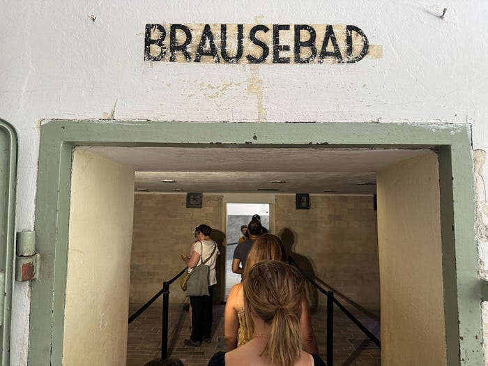 The back of a girl’s head as she crosses into the shower room at Dachau concentration camp, with the word “BRAUSEBAD” over her head (it means “shower” in German). The back of a girl’s head as she crosses into the shower room at Dachau concentration camp, with the word “BRAUSEBAD” over her head (it means “shower” in German).