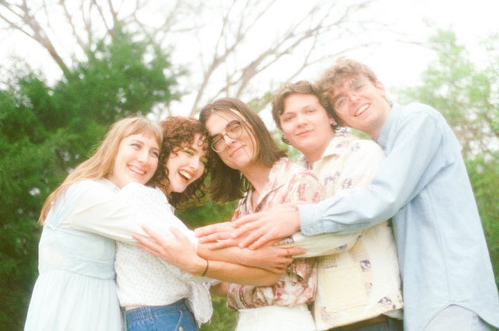 First image is a person with blonde hair surrounded by greenery and shadows. Second image is a group of four people standing together. Third image is of a person wearing glasses and playing guitar on a stage. Fourth image is of five people hugging in front of a wooded area. 