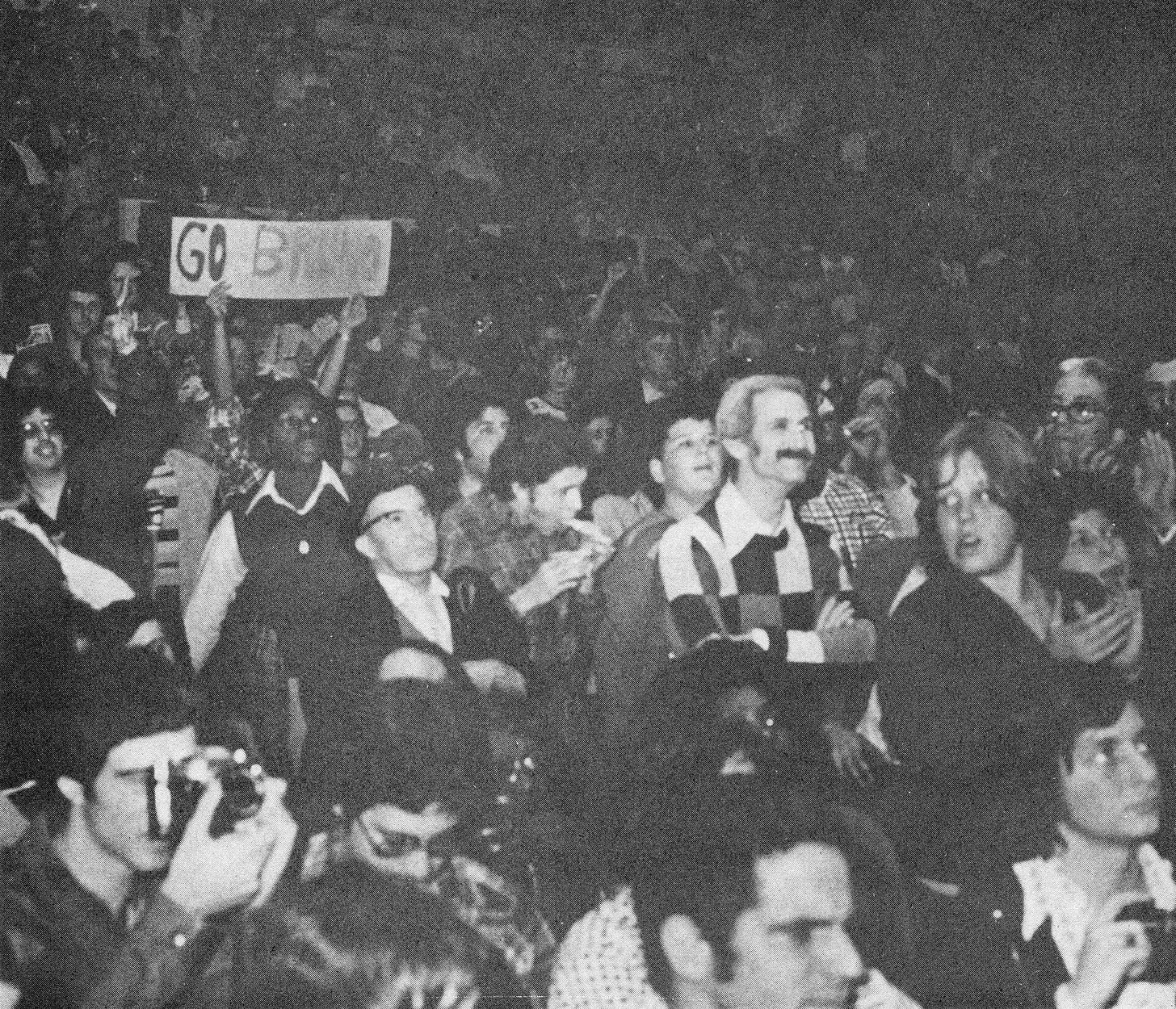 A black-and-white photo of a packed crowd at a 1975 wrestling show at Madison Square Garden, with a fan holding a hand-lettered Go Bruno sign