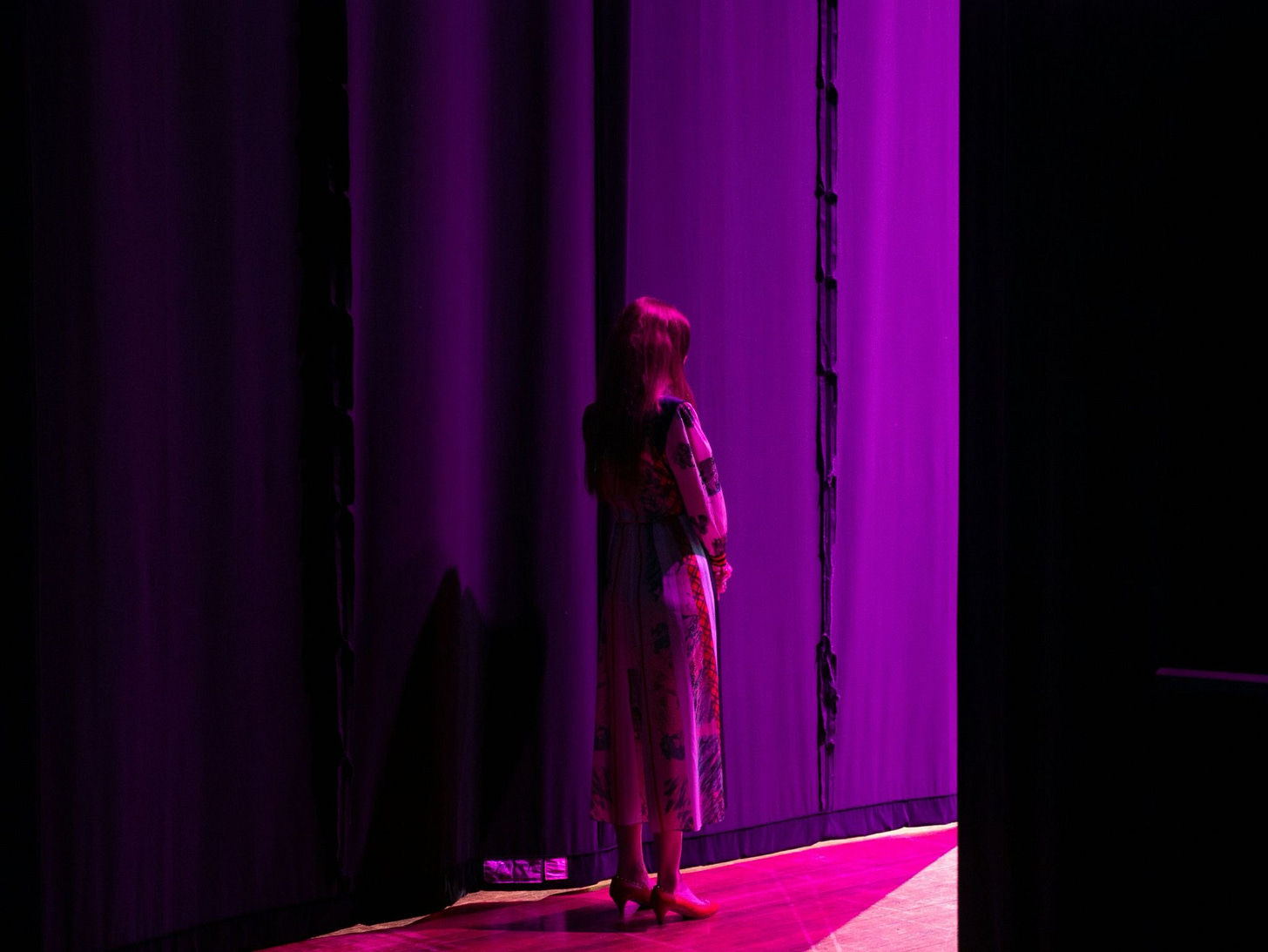 a woman standing in the wings of a stage lit in purple light a woman standing in the wings of a stage lit in purple light