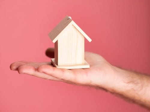 Free Wooden house model in hand symbolizing real estate concepts on pink background. Stock Photo