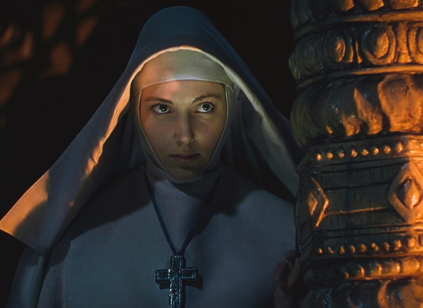 Sister Ruth in habit is peering from behind an ornate column at Sister Clodaugh and Mr. Dean. She's warmly but lingering in the shadows.