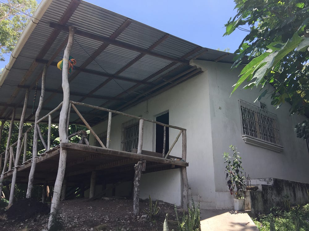 A white walled house has a metal roof over a large balcony.
