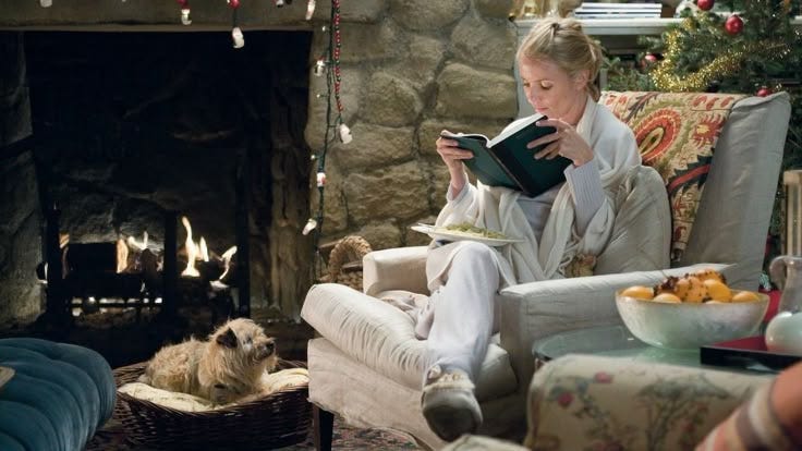 This may contain: a woman sitting on a chair reading a book in front of a fire place with christmas decorations This may contain: a woman sitting on a chair reading a book in front of a fire place with christmas decorations