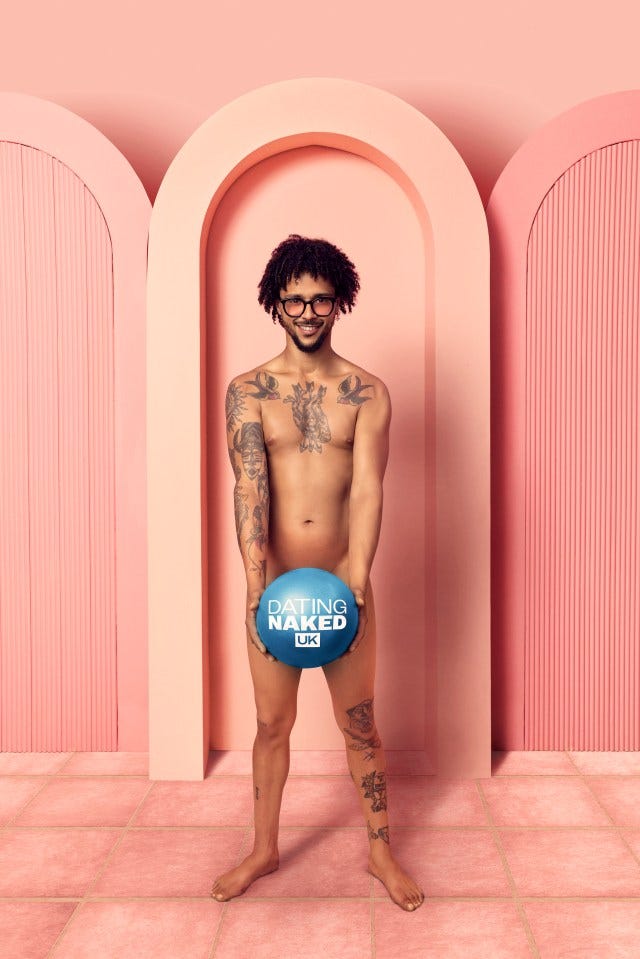 A tattooed man holds a ball that says "Dating Naked UK."