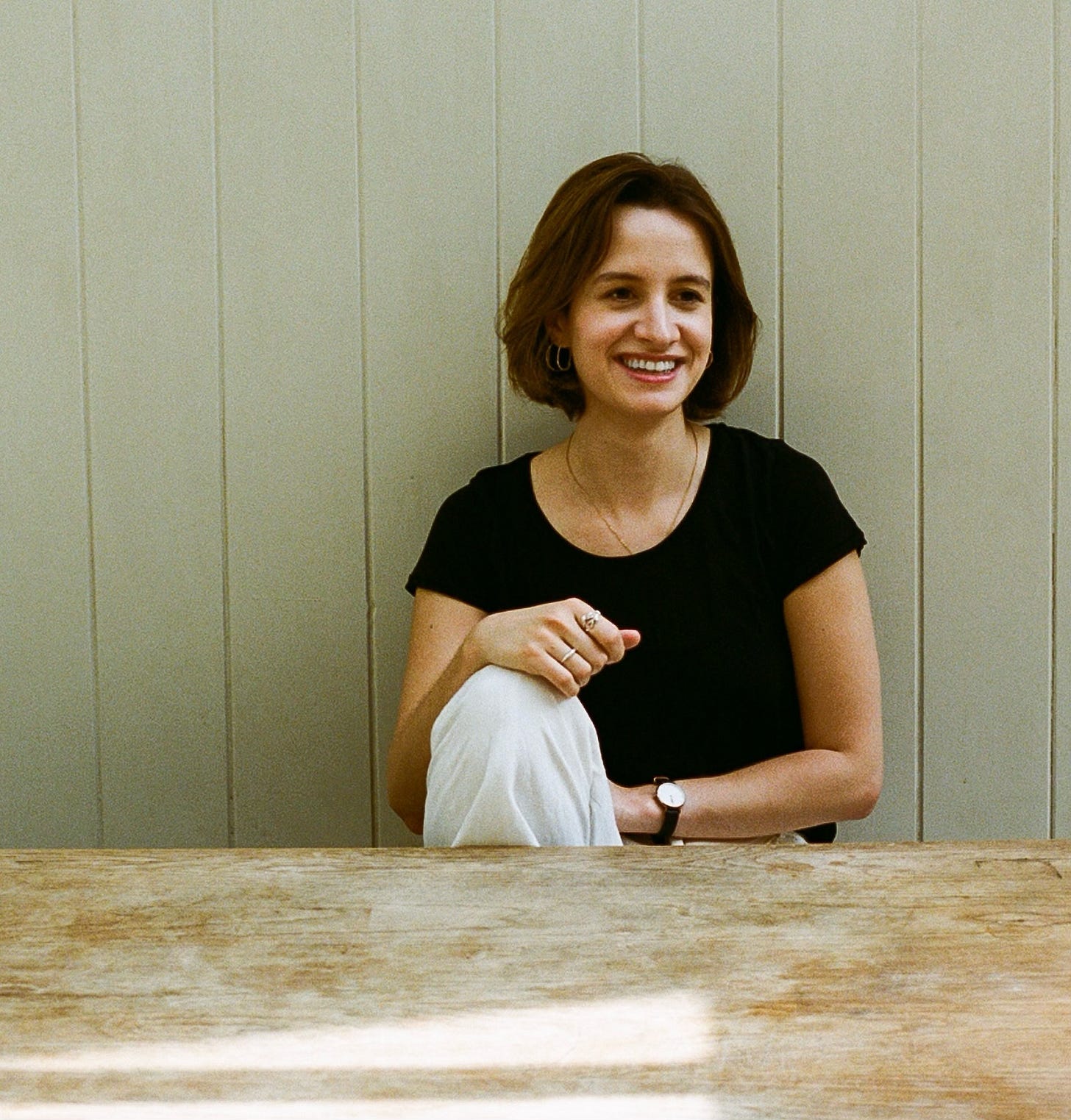 Celestine is a young white woman with bob cut brown hair. She’s dressed in a black round-neck T-shirt and white trousers and is smiling into the camera.