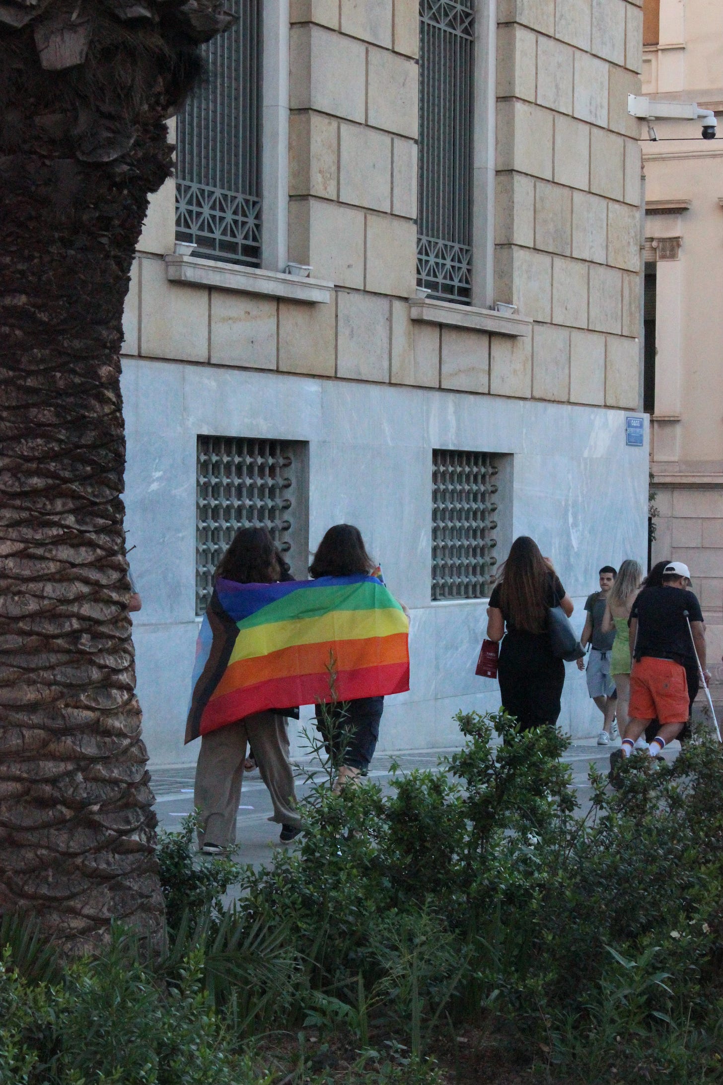 Δύο άτομα περπατάνε αγκαλιά με τη σημαία του Pride
