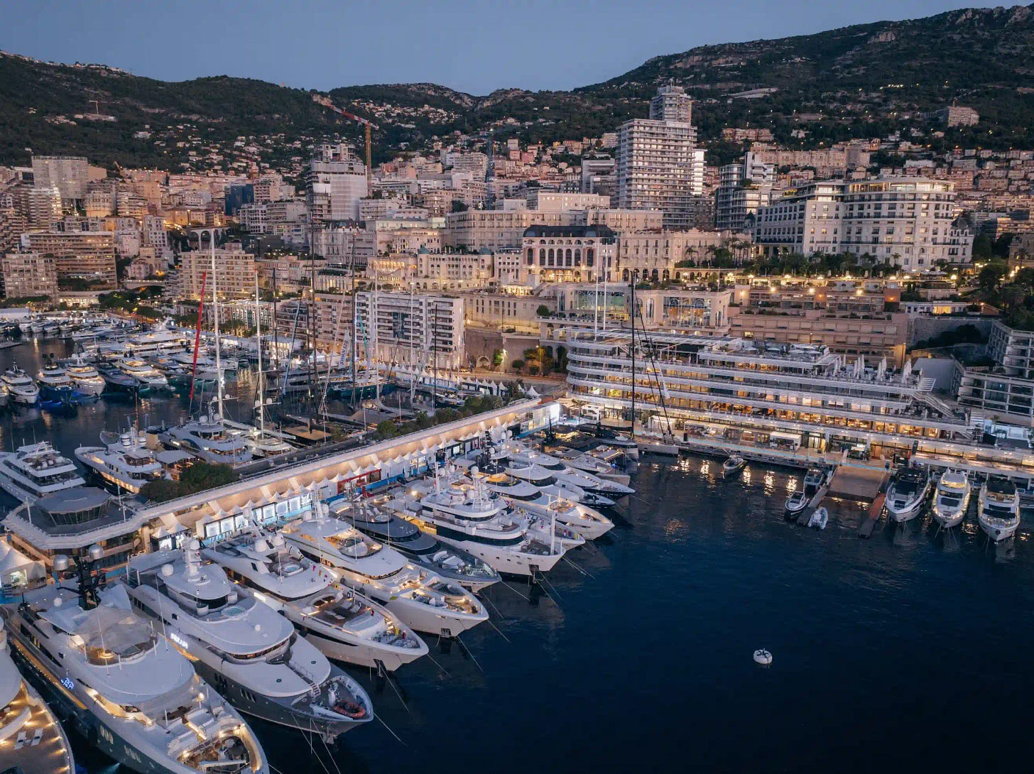 Evening panorama of the Monaco harbor illuminated by city lights and luxury vessels at dusk.
