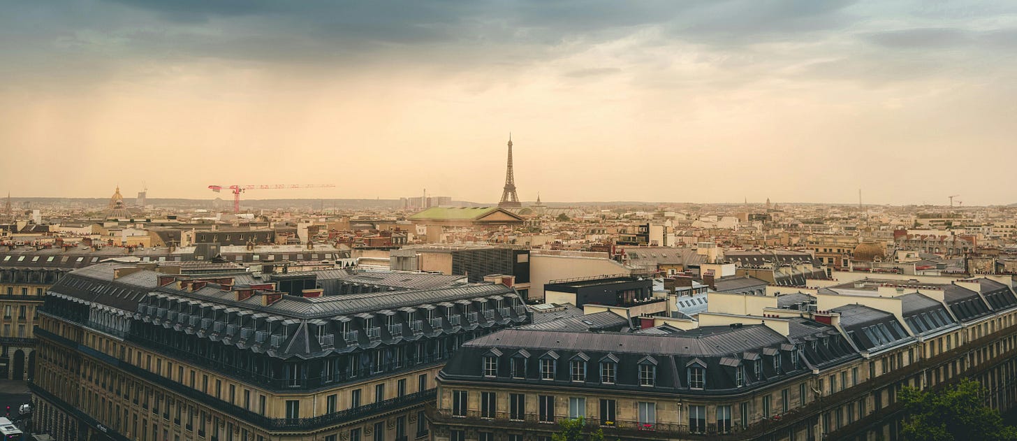 The rooftop of Paris, dark clouds above and the eiffel tower jutting into the sky in the middle of the scene. 