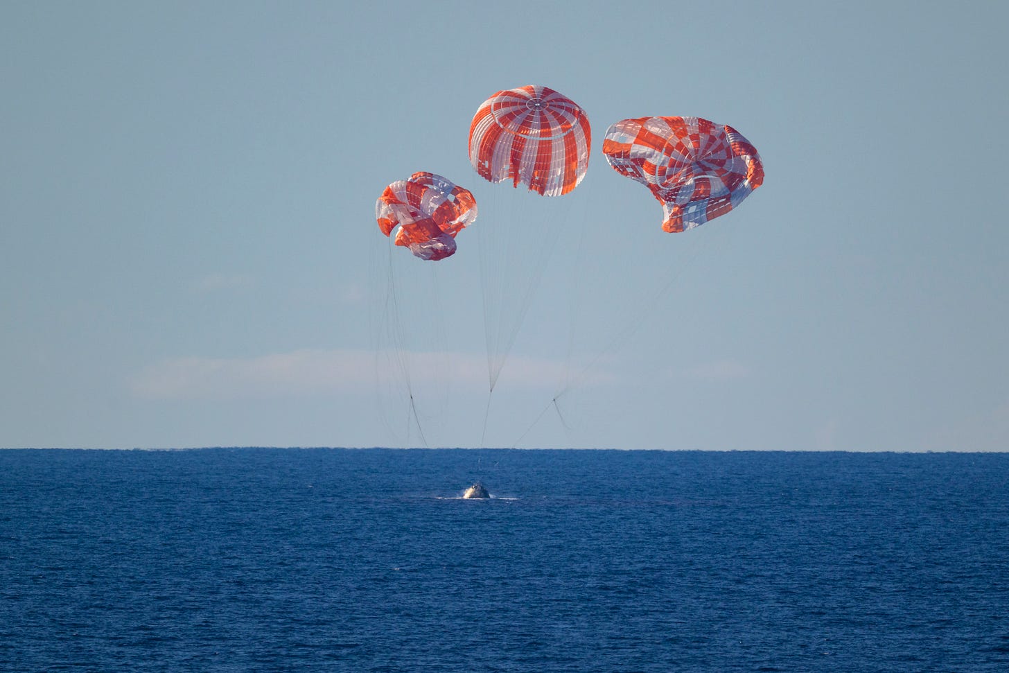 artemis II splashing down in the ocean, with three parachutes artemis II splashing down in the ocean, with three parachutes