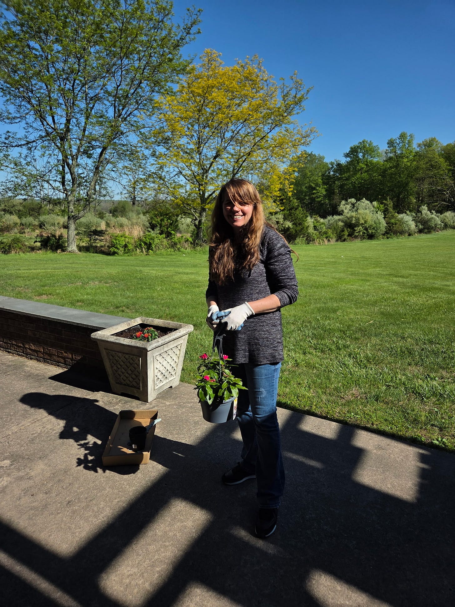 Photo of me holding the hanging vinca flowers basket with some red lantana flowers visible in the white planter behind me.