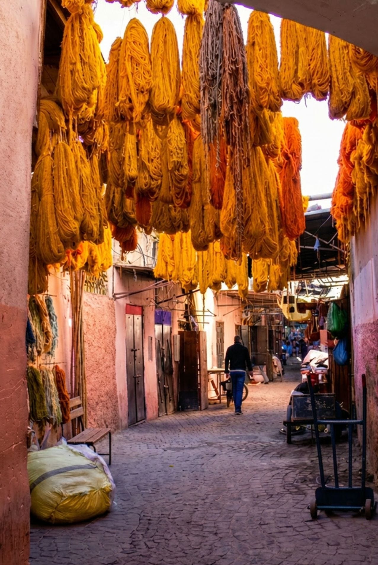 Bundles of dyed yellow and orange wool yarn hanging in a narrow, sunlit stone passageway of a Moroccan market. Bundles of dyed yellow and orange wool yarn hanging in a narrow, sunlit stone passageway of a Moroccan market.