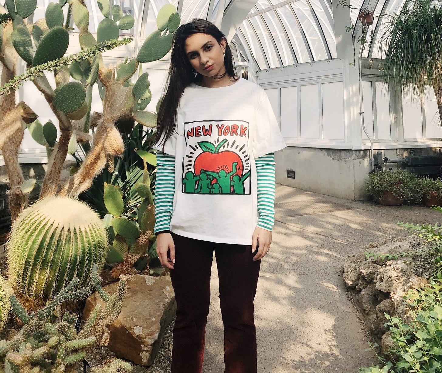 Portrait of Zaria Parvez standing in a cactus garden wearing a shirt that says "New York"
