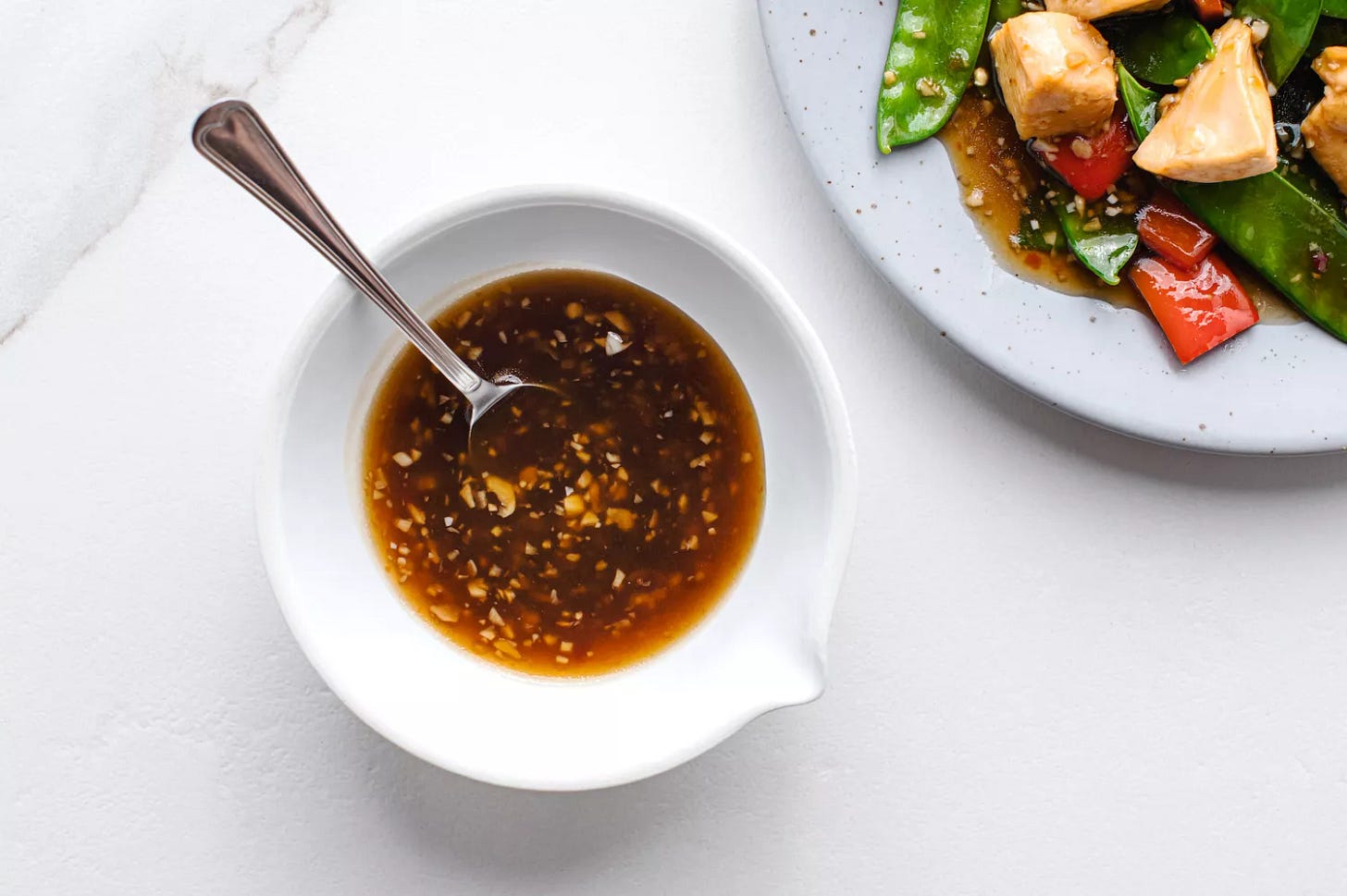 Chinese garlic sauce in a bowl next to a plate with a stir fry