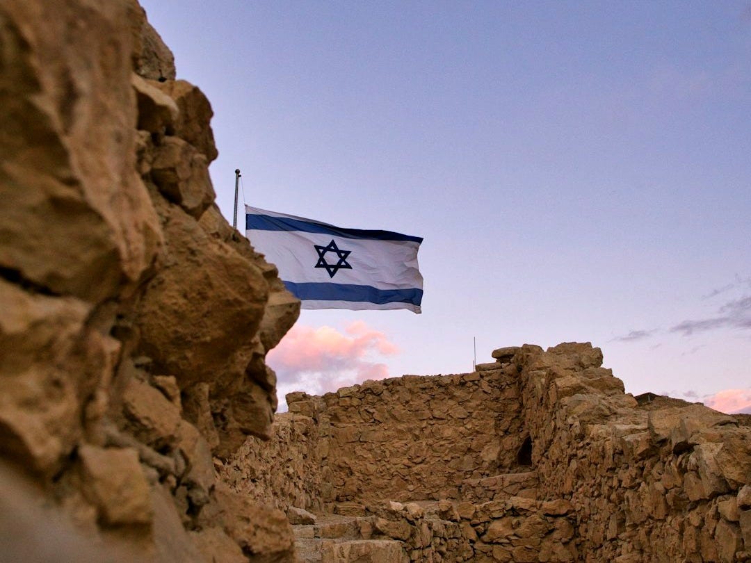 an israeli flag flying over a rocky area an israeli flag flying over a rocky area
