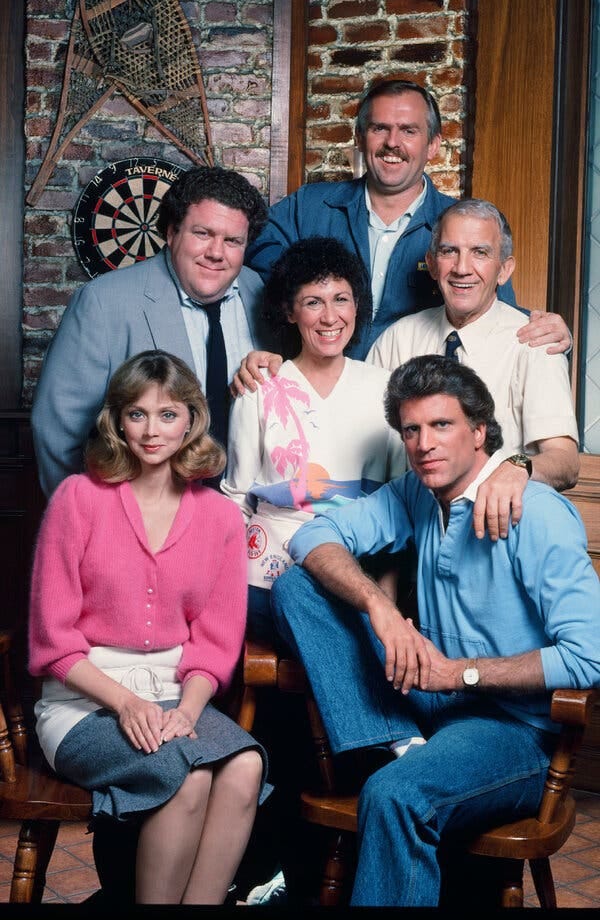 A group shot of the cast of “Cheers” on the show’s barroom set, in front of a brick wall.