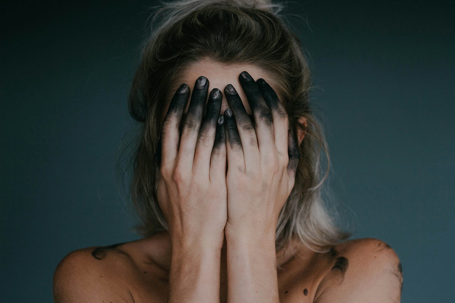 A woman with black fingertips covering her face.