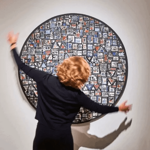 Woman pantomiming a clock in front of a painting.