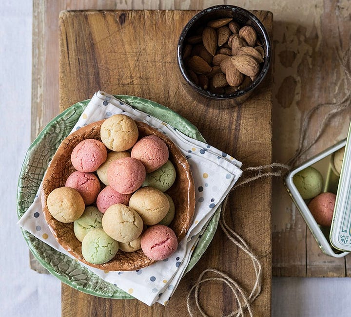 Delicate almond biscuits. One plate with natural ones, one plate of lightly coloured pastel, pink, green & brown