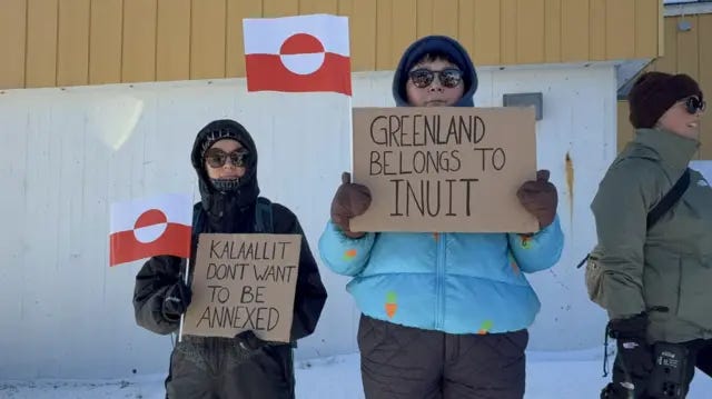 Two people dressed in heavy jackets, sunglasses and mittens at an anti-US protest in Greenland. They are holding indigenous red and white flags and signs that read "Kalaallit don't want to be annexed" and "Greenland belongs to Inuit". Two people dressed in heavy jackets, sunglasses and mittens at an anti-US protest in Greenland. They are holding indigenous red and white flags and signs that read "Kalaallit don't want to be annexed" and "Greenland belongs to Inuit".
