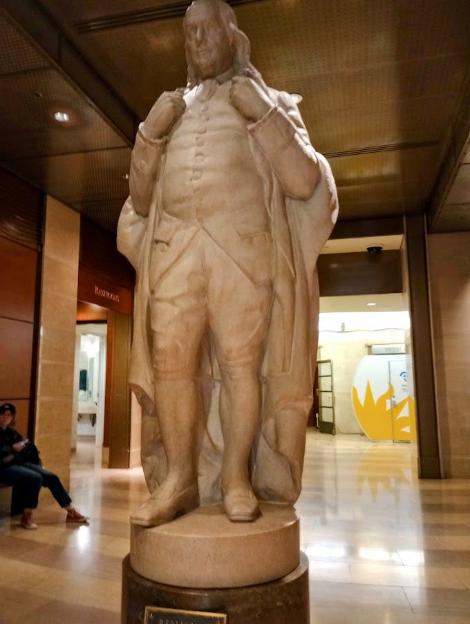 Left, statue of man in robes. Right, plaque explaining Franklin's accomplishments