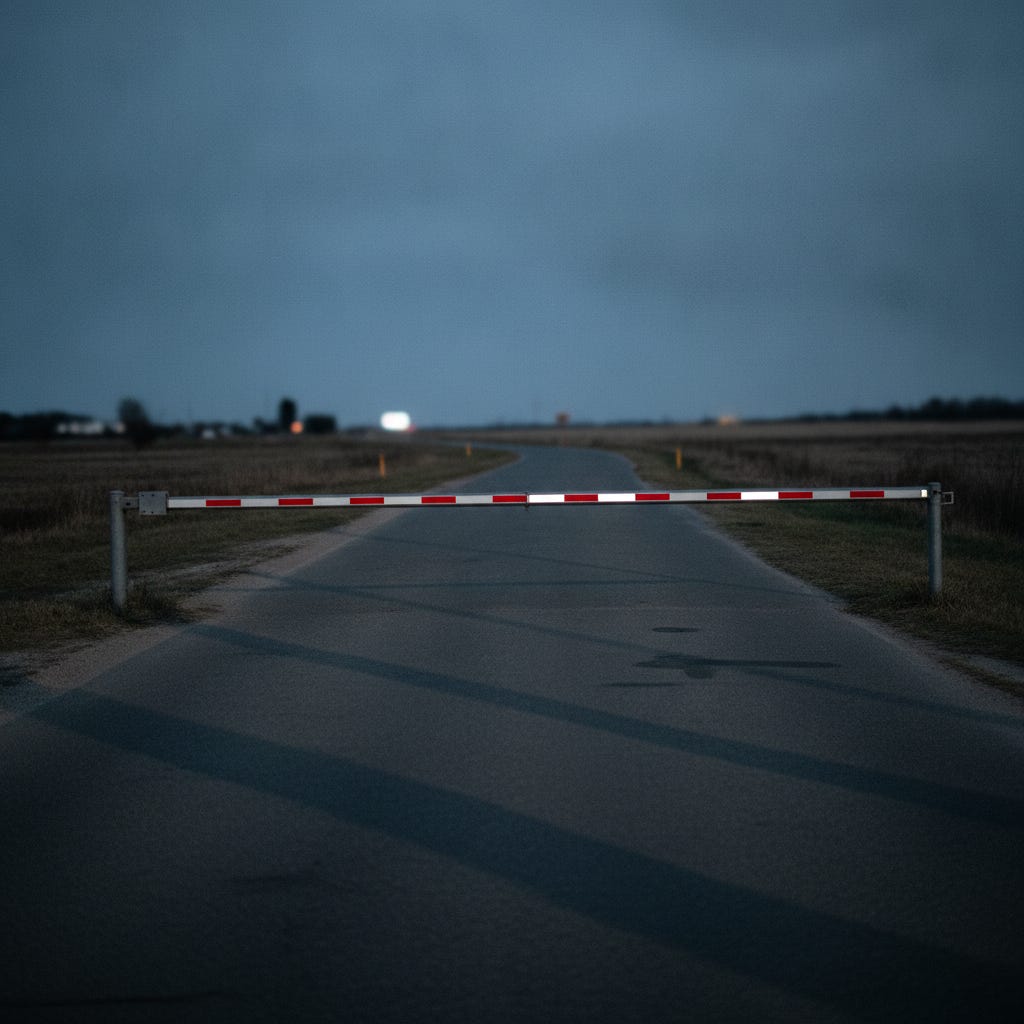 A gate arm lowered across an empty road, with open ground on both sides of it