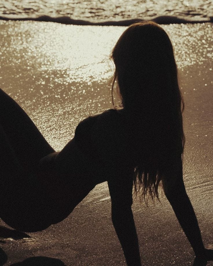 This may contain: a woman is sitting on the beach with her legs spread out and feet in the water