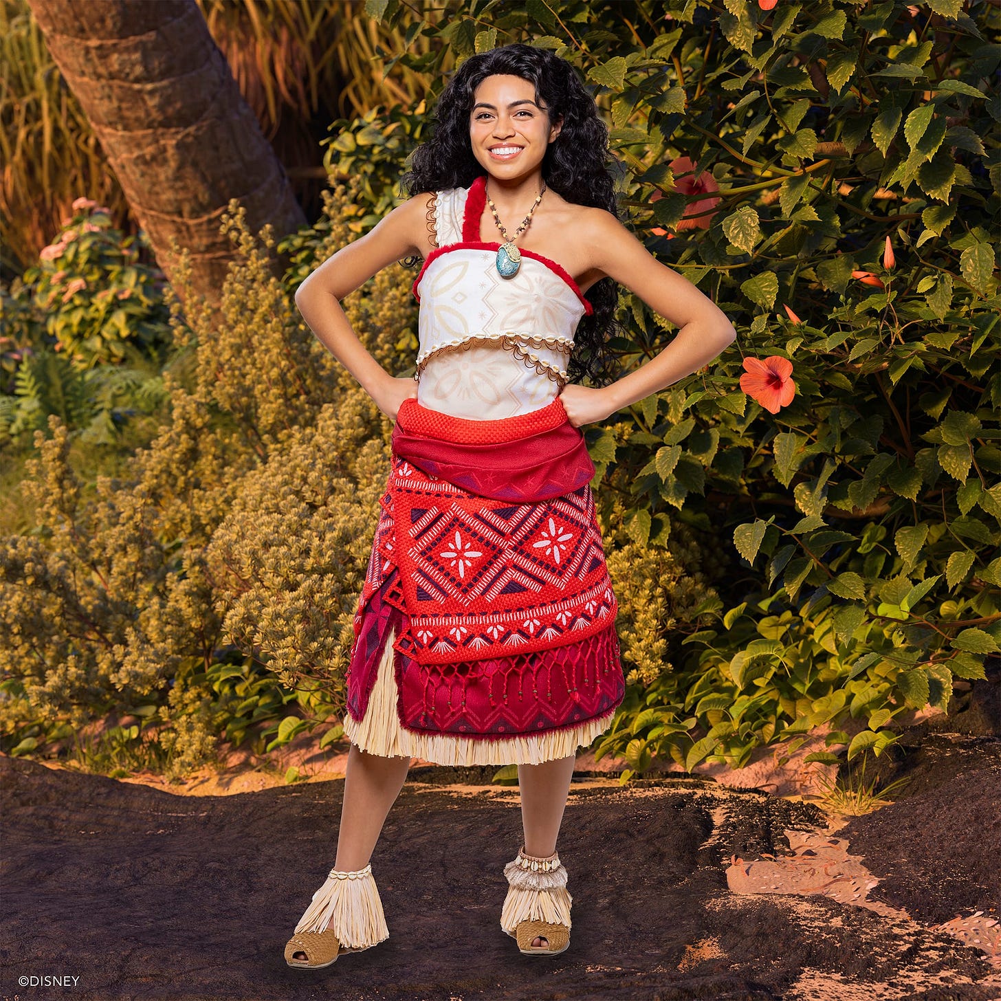 Amidst lush greenery, a person in traditional Polynesian attire stands beside a large hibiscus flower, evoking the spirit of Moana in a scene reminiscent of Disney Parks' enchanting meet and greet experiences.