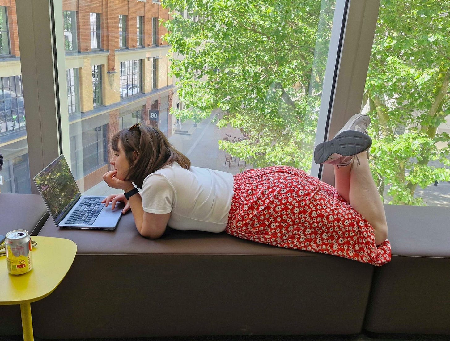 Chloe lying on some couches, working on a laptop, Diet Coke within reach.