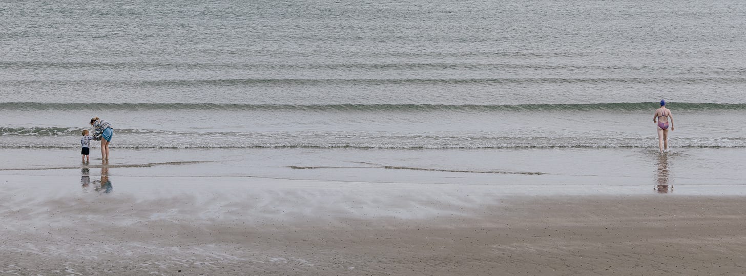 A wide pale strand at low tide, two small figures at the left edge and a single bather far off to the right, sand and water almost merging. A wide pale strand at low tide, two small figures at the left edge and a single bather far off to the right, sand and water almost merging.