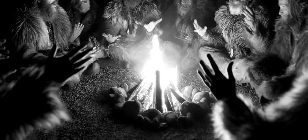 A wide-angle scene depicting a group of ancient people dressed in fur clothing, gathered around a campfire at night. They are carrying primitive stone spears and their faces are warmly illuminated by the flickering firelight. The group is engaged in storytelling, with animated gestures and expressions, creating a sense of camaraderie. The composition is minimalist, focusing solely on the people and the fire, with a dark, starless night as the backdrop. The scene is designed as if shot with a Nikon Z7 II and a 35mm f/1.8 lens, using a warm and earthy color palette to emphasize the firelight and natural tones of their clothing and surroundings.