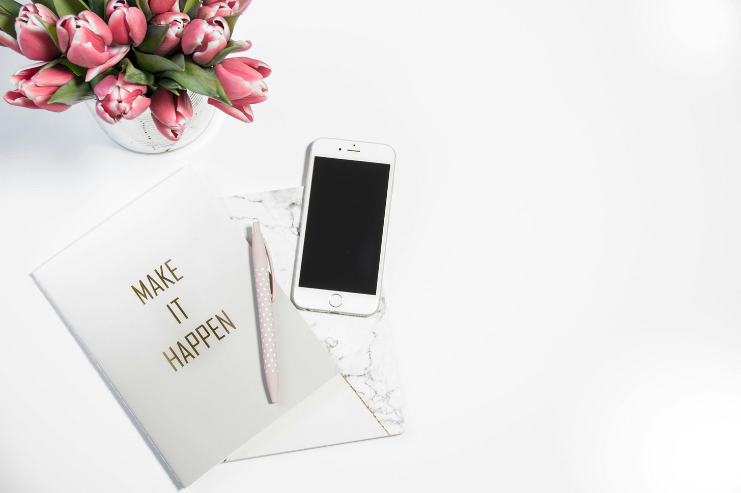 Smart phone, pen, and notebook on a desk. Notebook cover says "make it happen". Smart phone, pen, and notebook on a desk. Notebook cover says "make it happen".
