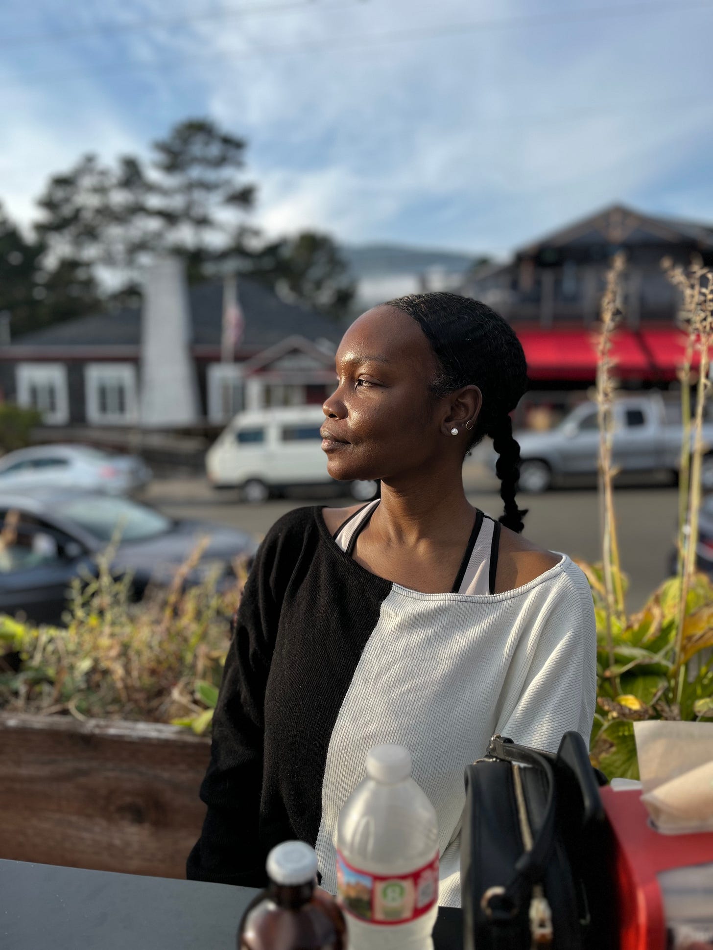 Nafissa sits at a table outdoors. She is in profile, looking to the side as the sun hits her face, making her glow.