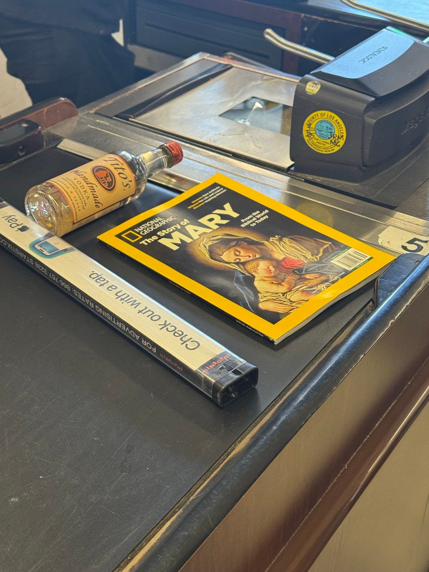 someone buying a bottle of Tito's vodka and a NatGeo issue about the story of the Virgin Mary